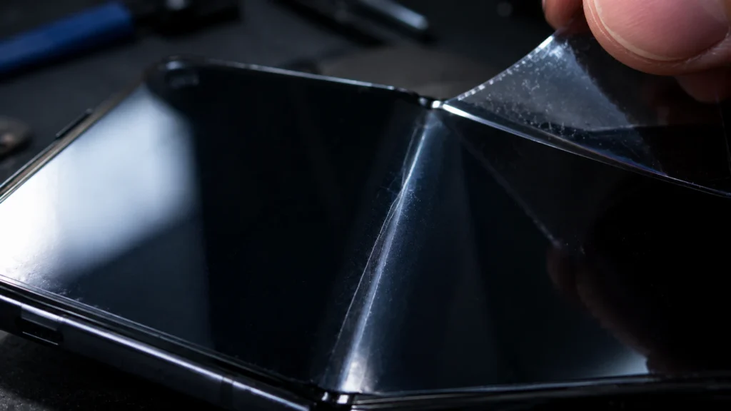 "Macro shot of foldable phone crease showing a stress line under a bubbled screen protector on the display panel"