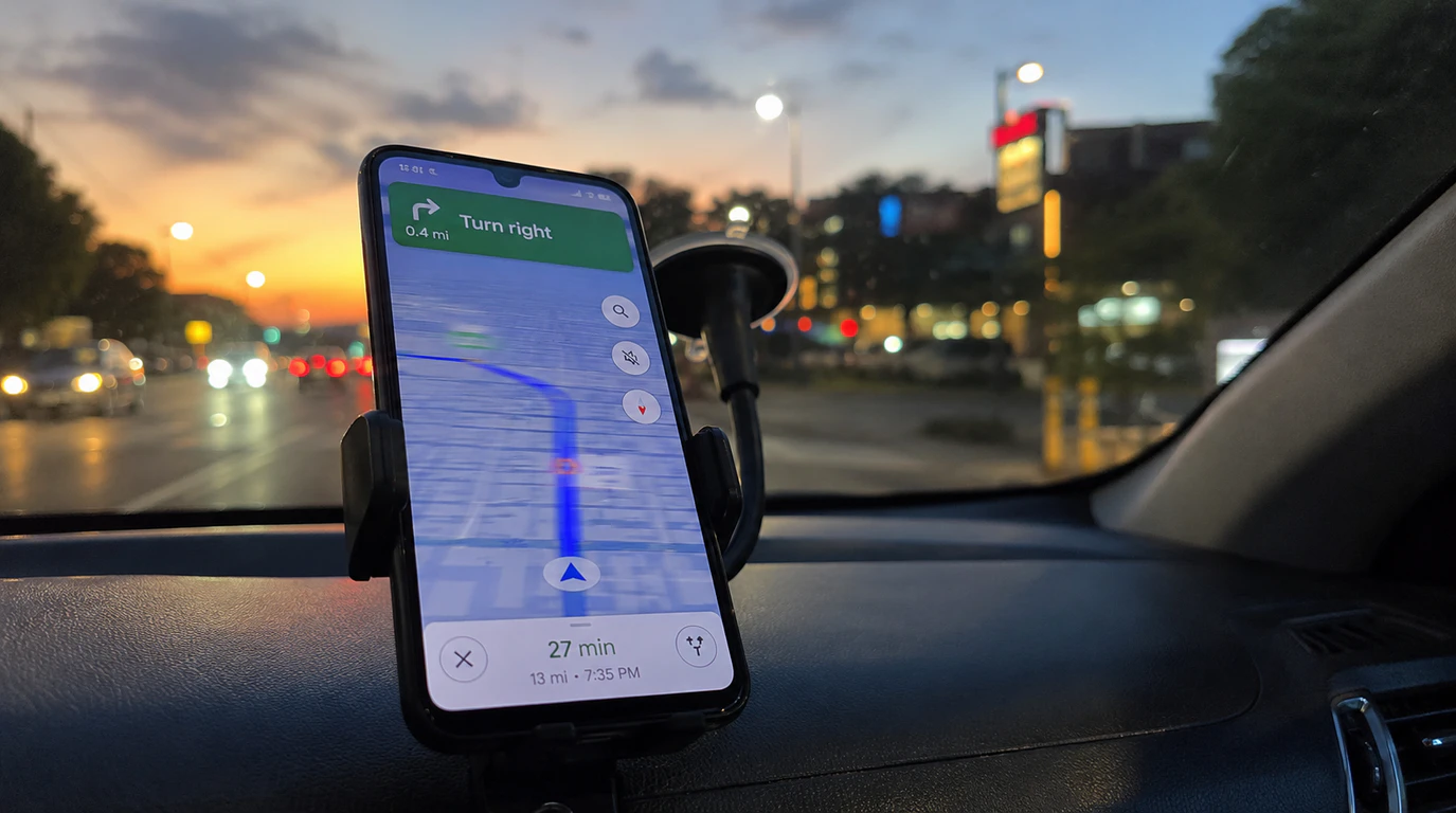 Smartphone mounted on a car dashboard showing a frozen Google Maps navigation screen while driving at dusk